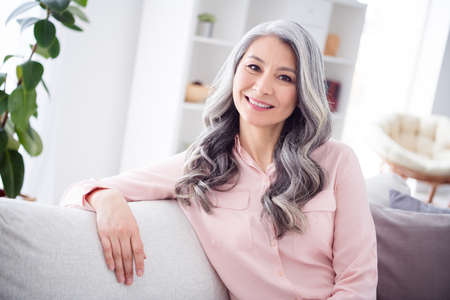 Photo of happy positive nice charming old woman sit couch good morning smile indoors inside house homeの写真素材