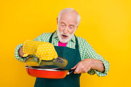 Portrait of attractive curious elderly trendy cheerful grey-haired man frying tasty dish meal recipe isolated over bright yellow color backgroundの写真素材