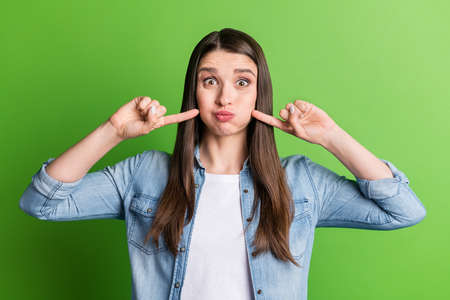 Portrait of attractive cheerful funky girl pressing cheek holding air isolated over bright green color backgroundの写真素材