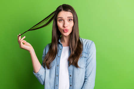 Portrait of attractive cheerful girl playing with hair pouted lips good mood isolated over bright green color background