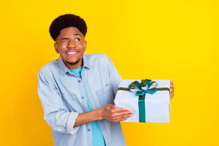 Photo of excited flirty dark skin guy dressed denim shirt smiling holding present box looking empty...