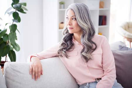 Portrait of pretty focused aged person sit on sofa look interested window thinking free time weekend...