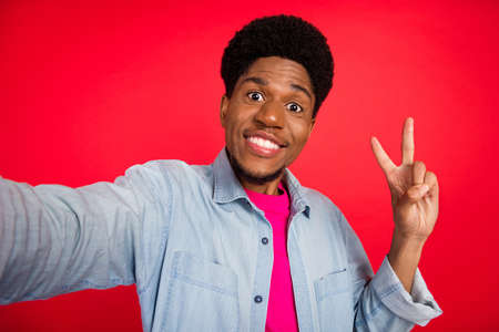 Photo of young black guy happy positive smile shoot selfie show peace cool v-sign isolated over red color backgroundの写真素材