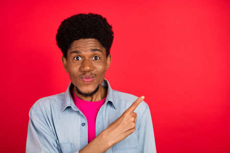 Photo of young african guy happy positive smile point finger empty space ad promo choose isolated over red color backgroundの写真素材
