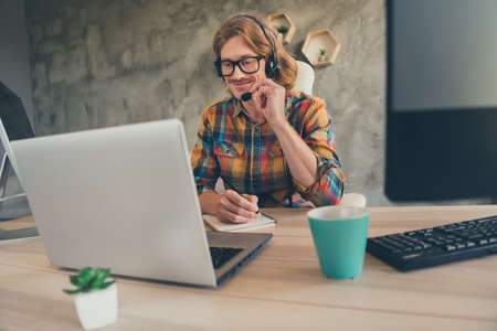 Photo of young guy happy positive smile speak conversation speaker headphone write plan manager computer indoorsの写真素材