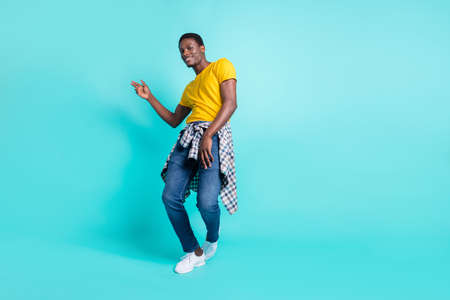 Full length photo of nice brunette hairdo millennial man dance wear yellow t-shirt jeans sneakers isolated on cyan color backgroundの写真素材