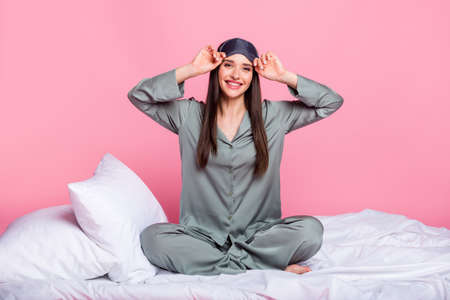 Photo of pretty shiny young woman nightwear smiling sitting duvet isolated pastel pink color...