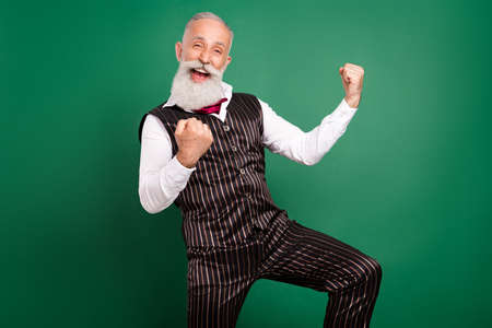 Photo of positive imposing bearded senior man raise fists open mouth wear striped suit on green color backgroundの写真素材