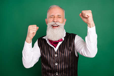 Photo of excited cheerful senior well-groomed man raise fists wear striped suit on green color...