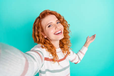 Photo portrait of red haired girl in striped sweater smiling taking selfie showing empty space isolated vivid teal color backgroundの写真素材