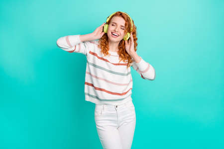 Photo portrait curly woman smiling listening music in earphones overjoyed isolated vibrant turquoise color backgroundの写真素材