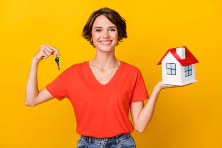 Photo of nice brunette optimistic lady hold house keys wear red t-shirt isolated on vivid yellow color backgroundの写真素材