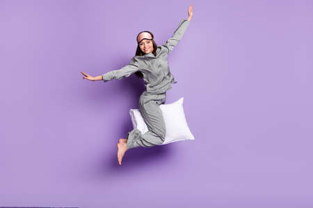 Full length body size photo of cheerful woman riding on pillow wearing grey pajama isolated on...