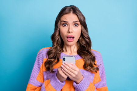 Portrait of impressed person hold phone open mouth staring camera wear pullover isolated on blue color backgroundの写真素材