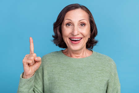 Photo of elder grey hair funky lady index up wear green jumper isolated on blue color background