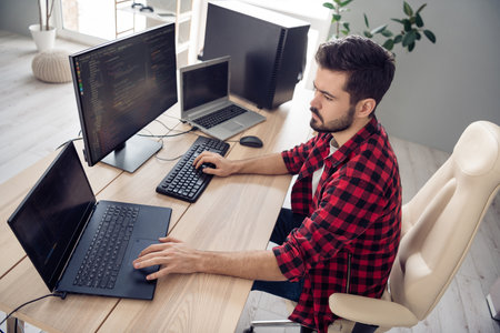 Photo of concentrated serious young man walk programmer write code pc sit table inside indoors...