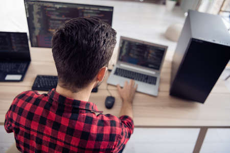 Back rear spine view photo of young man sit desk work code develop software write indoors inside...
