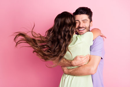 Portrait of attractive dreamy affectionate cheerful couple embracing wind blowing hair isolated over pink pastel color backgroundの写真素材