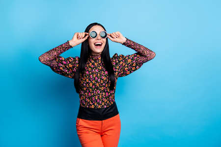 Photo of amazed excited young woman look empty space wear cool sunglass isolated on blue color backgroundの写真素材