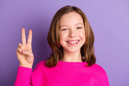 Photo of positive sweet cute small schoolgirl make v-sign good mood isolated on purple color...