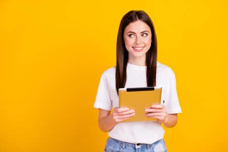 Photo of young girl happy positive smile hold tablet gadget look empty space isolated over yellow color backgroundの写真素材
