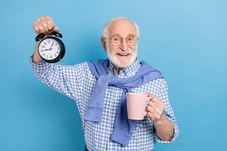 Photo of optimistic old grey hairdo man hold clock cup wear spectacles blue shirt isolated on pastel...