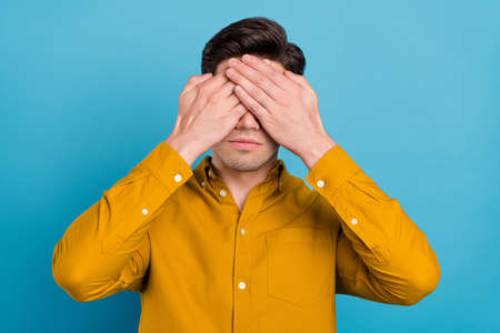 Photo of serious unhappy young man wear yellow shirt arms cover eyes having headache isolated blue color backgroundの写真素材