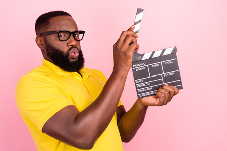 Photo of afro american brown haired man wear glasses yellow t-shirt hold clapper glasses isolated on pink color backgroundの写真素材