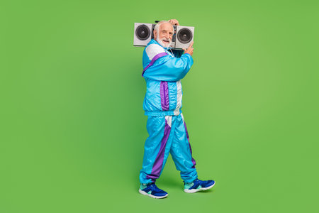 Photo of pretty charming senior man wear sportive suit listening boombox smiling isolated green color backgroundの写真素材
