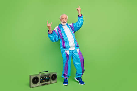 Photo of funky cool senior man wear sportive suit listening boombox showing hard rock sign smiling isolated green color backgroundの写真素材