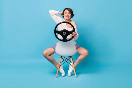 Photo portrait full body view of scared woman holding steering wheel sitting on reversed chair isolated on pastel blue colored backgroundの写真素材