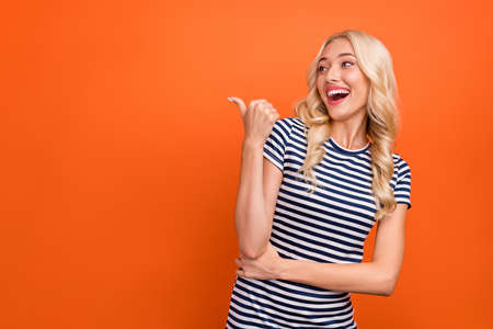 Photo portrait blonde woman wearing striped t-shirt pointing copyspace with thumb isolated vivid...