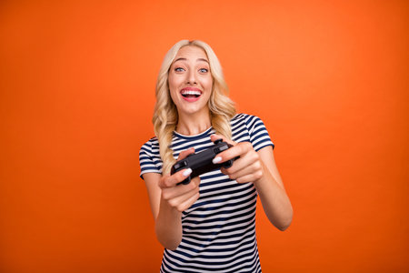 Portrait of attractive addicted cheerful girl playing game having fun pastime isolated over bright orange color backgroundの写真素材