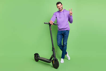 Full body photo of young cheerful man happy positive smile ride scooter show peace v-sign isolated...