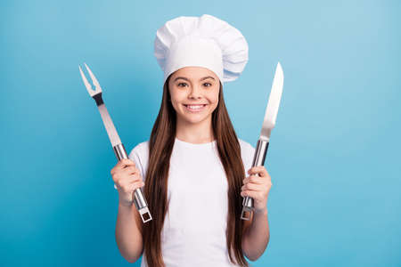 Photo of cheerful positive happy little girl smile good mood hold knife fork lunch isolated on blue color backgroundの写真素材