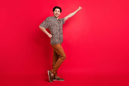 Full size profile side photo of young funky smiling positive hold hand waist isolated on red color backgroundの写真素材