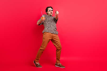 Full size photo of good mood amazed surprised man dancing drink cocktail point finger you isolated on red color backgroundの写真素材
