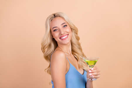 Profile side photo of young cheerful woman happy positive smile drink cocktail glass isolated over beige color backgroundの写真素材