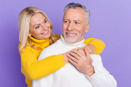 Photo of adorable cute mature wife husband wear knitted pullovers smiling embracing looking eyes isolated purple color backgroundの写真素材