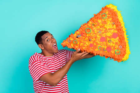 Photo of funky funny young man wear striped t-shirt smiling biting huge pizza slice isolated teal color backgroundの写真素材