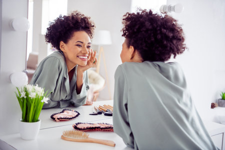 Portrait of attractive cheerful girl looking at mirror applying daily cream at light white home indoorsの写真素材