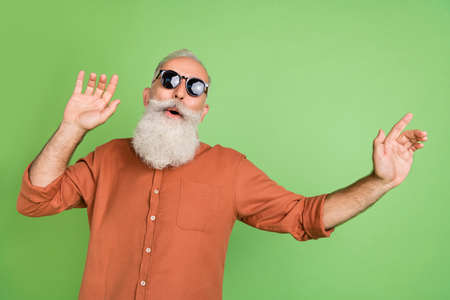 Portrait of attractive funny cheerful grey-haired man enjoying dancing having fun rest isolated over green color backgroundの写真素材