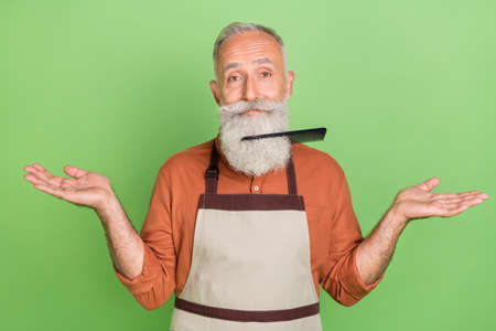 Photo of mature man hairdresser brush stack in beard clueless puzzled isolated over green color...
