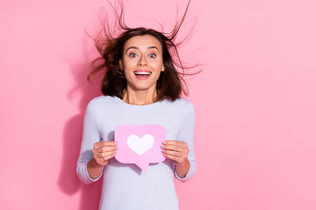 Photo of carefree excited young woman wear white sweater holding notification heart like sign empty...