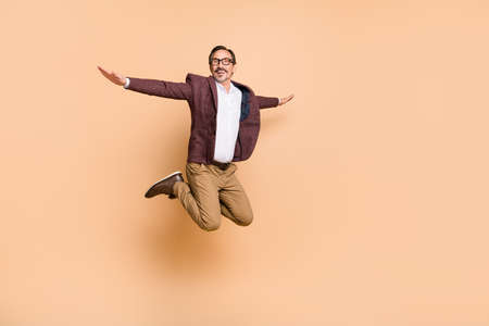 Full length body size view of attractive cheery carefree man jumping flying like plane isolated over beige color backgroundの写真素材