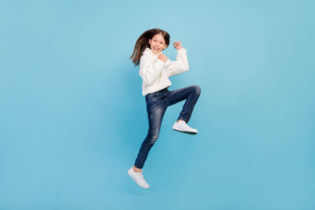 Photo of funky lucky preteen girl dressed white pullover rising fists jumping high smiling isolated...
