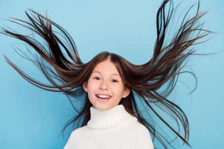 Photo of shiny pretty preteen girl dressed white pullover flying hair smiling isolated blue color backgroundの写真素材