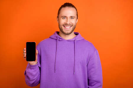 Photo of lovely young brown hairdo guy show telephone wear violet pullover isolated on orange color backgroundの写真素材