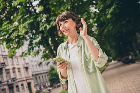 Photo of funny cute young lady dressed green shirt walking typing modern gadget waving arm smiling...