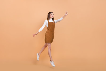 Full body profile portrait of active cheerful girl raise arm look empty space isolated on beige color backgroundの写真素材
